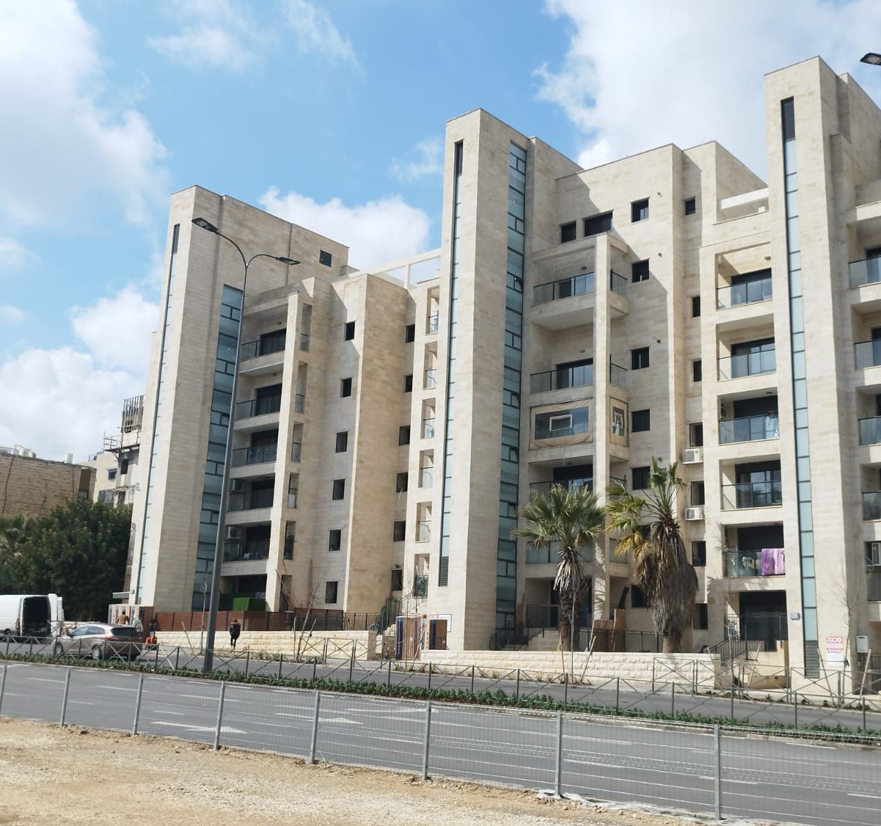 A modern Jerusalem stone apartment building with palm trees at the entrance